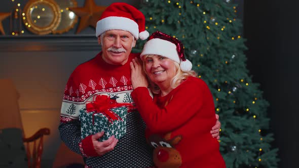 Senior Couple Family in Santa Claus Hats Celebrating Christmas Looking at Camera and Hugging at Home