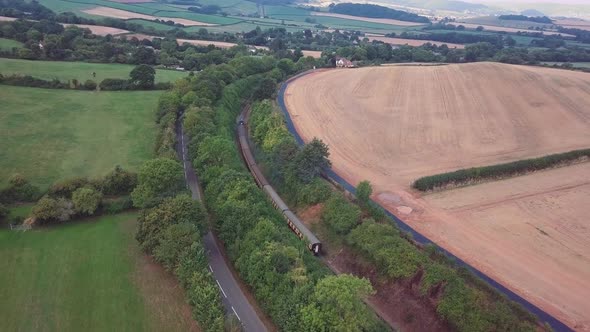 Aerial tracking forward towards a steam train that ising away from the camera around a tight bend su