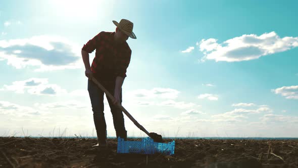 Farmer Digging Soil with Shovel in Rubber Boots in Garden Field at Sunset Spring