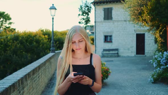 Charming Young Woman Using Smartphone While Walking Outside in Summer