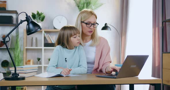 Mother in Glasses Sitting Together with Her 12-Aged Cute Daughter and Helping Her with Home Task