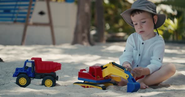 Children Plays with a Plastic Car in the Sand on the Beach