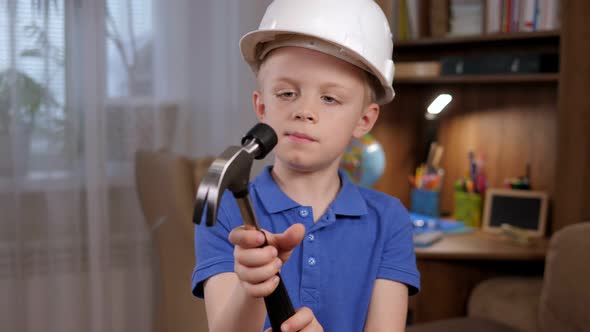 Portrait of a Little Boy in a White Helmet with a Hammer in His Hands at Home