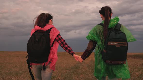 Happy Girls in Colored Raincoats Travel with Backpacks
