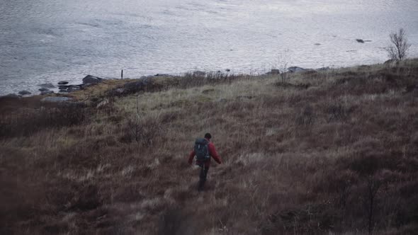 Hiker Walking In Grass Towards Fjord