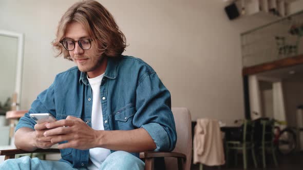 Cheerful blond man in eyeglasses texting on phone