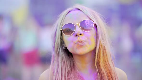 Girl in Sunglasses Covered in Colorful Dyes Smiling, Blowing Air Kiss to Camera