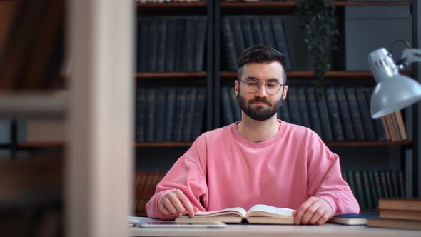 Successful Clever Man Posing at Public Library Desk with Open Paper Book Smiling Enjoying Break