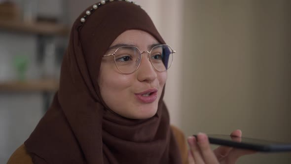 Closeup of Confident Middle Eastern Woman in Eyeglasses and Hijab Talking in Speakerphone Indoors