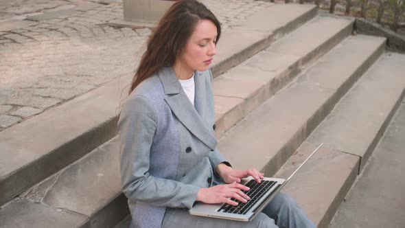 Young Woman Sitting on Stairs While Using Laptop on the Street