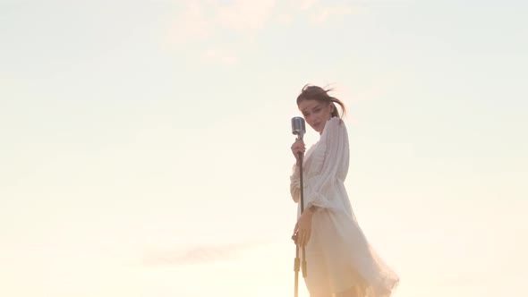 Beautiful Woman in White Dress on Top of Mountain on Edge of Abyss and Sings Song Into Shiny Retro