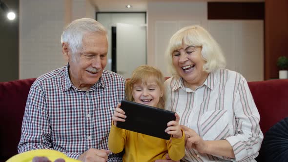 Senior Caucasian Couple with Cute Child Girl Granddaughter Using Tablet, Watching Funny Videos