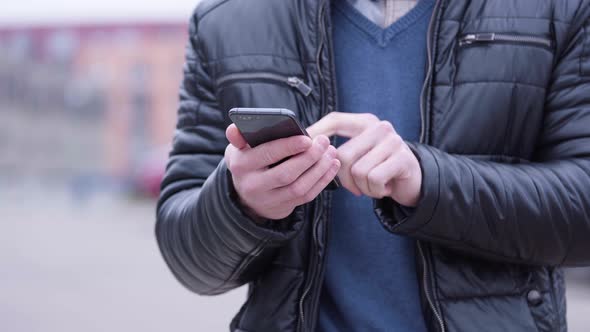 A Man Works on a Smartphone - Front Closeup - Suburban Area in the Blurry Background