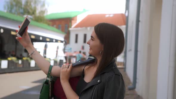 A young pretty girl makes a video call to her friend on the phone from the old town.	