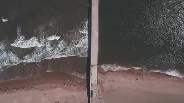 Aerial birds eye view drone footage of a waves crashing onto the beach against a pier, Roker Beach,