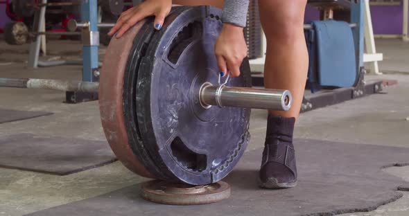 Female weight lifter taking weights off her lifting bar at the gym