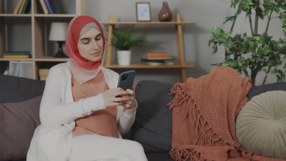 Pregnant Arabian Woman in Hijab Using Mobile Phone at Home