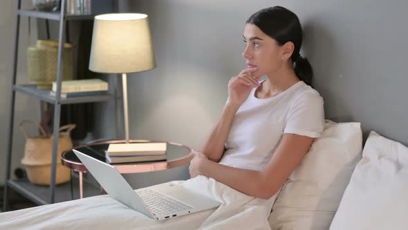 Young Latin Woman with Laptop Thinking in Bed