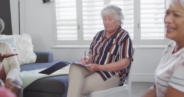 Caucacian senior female counsellor with clipboard advising to group of diverse senior friends