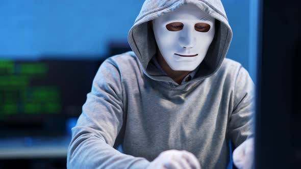 Confident Anonymous Hacker in Face Mask Typing on Keyboard in Blue Office