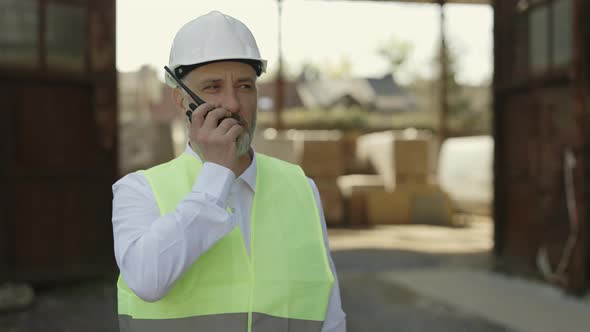 Man Walking Around Construction Site and Using Walkie Talkie