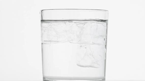 Ice cubes spin in glass of water over white