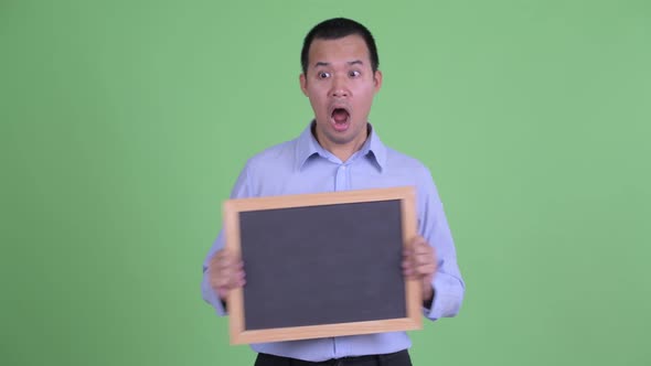 Happy Asian Businessman Holding Blackboard and Looking Surprised
