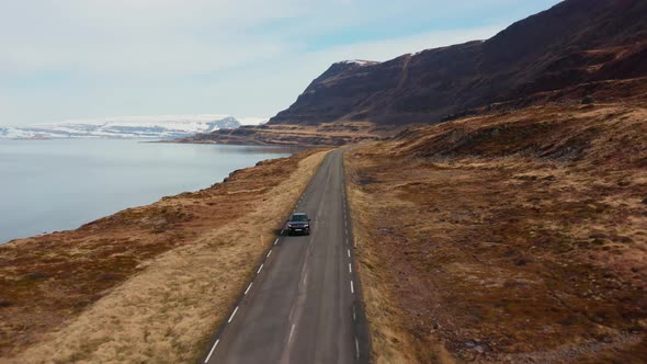 Drone Tracking Car Driving By Fjord Away From Mountains