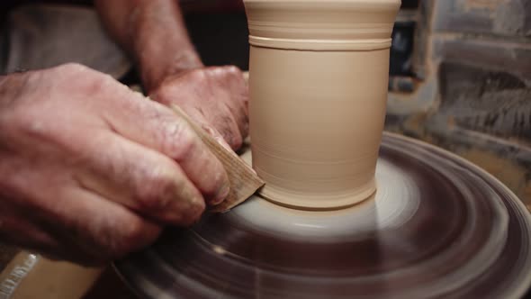 Potter Rotates Wet Clay Product on Potter's Wheel and Makes Design Using Wooden Scraper
