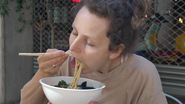 Healthy Vegan Asian Cuisine. Hungry Caucasian Girl Eating Vegan Ramen Soup with a Big Pleasure. 