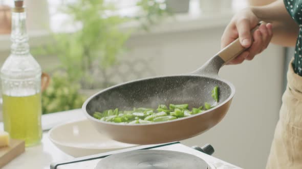 Unrecognizable cook frying green beans in pan