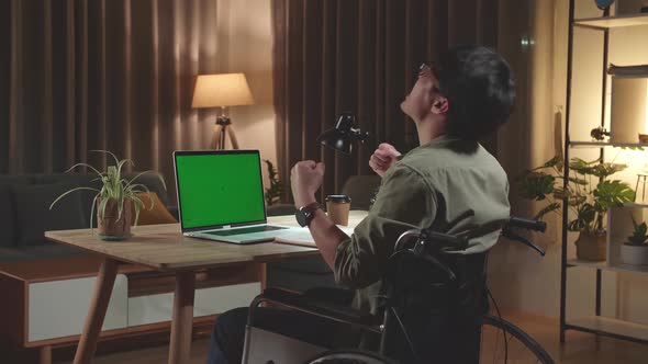 Asian Man Sitting In A Wheelchair While Working On Green Screen Laptop And Celebrating At Home