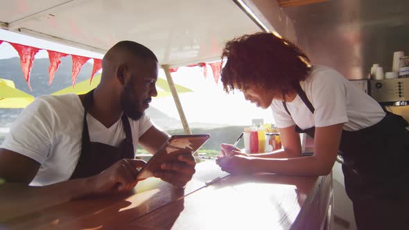 African american couple wearing aprons using digital tablet and taking notes in the food truck