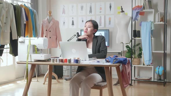 Asian Female Designer In Business Suit Working On A Laptop And Thinking While Designing Clothes