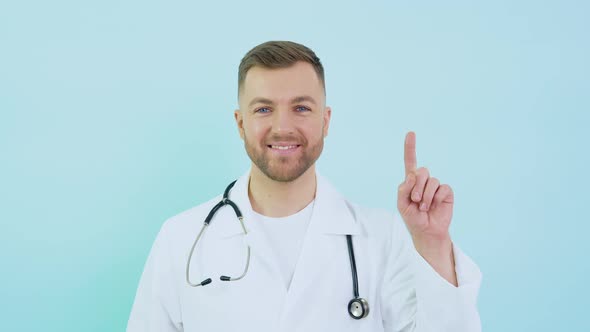 Doctor with Stethoscope in White Coat Raises His Index Finger Up to Face Level on a Blue Background