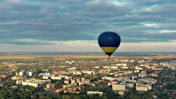 Multicolored balloons fly over fields, houses, trees. Blue sky.