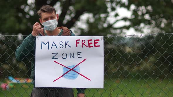 A Poster on the Fence with the Inscription Mask Free Zone. A Young Male Activist Comes Up and Takes