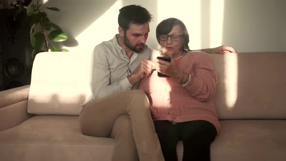 Grandson Teaching Old Granny Using Mobile Phone.Older Women Fun With Grandson Looking On Smartphone.