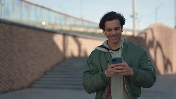 Smiling Man in Earphones Walking with Mobile in Hands