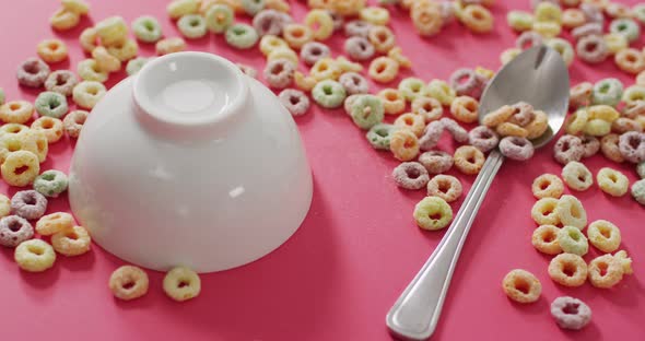 Video of colorful breakfast cereals with bowl and spoon on pink background