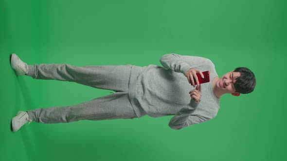 Full Body Of Asian Man Enjoy Using Mobile Phone While Standing On Green Screen In The Studio