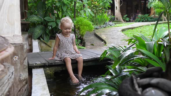 Joyful Charming Blonde Kid Playing with Water in a Hotel Decorative Pond Smiling Innocent Happiness