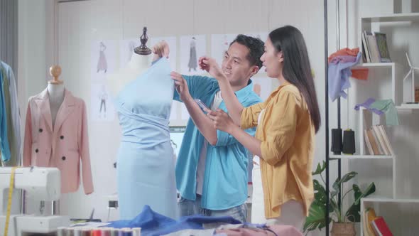 Asian Male And Female Designers Comparing A Dress On A Mannequin To The Pictures On Smartphone