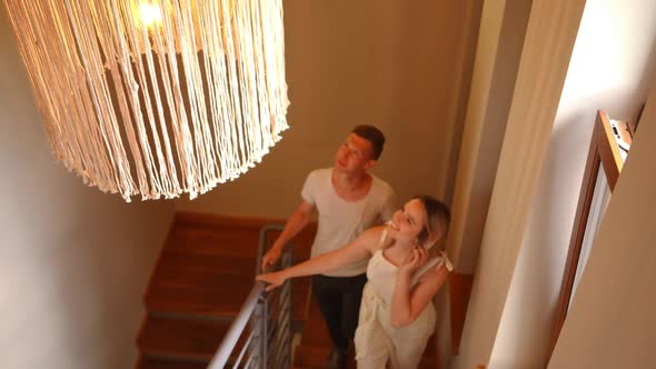 Closeup Lamp Shining in Lampshade with Cheerful Young Couple Walking Upstairs at Background