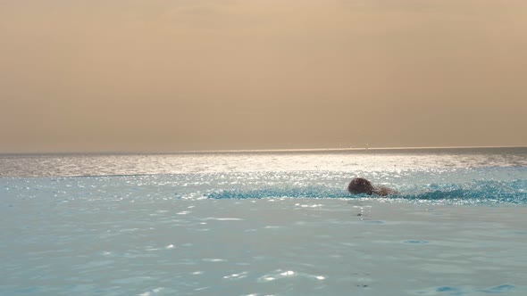 Man Swims Skillfully, with a Stroke, Works Out Technique in Outdoor Infinity Pool with Panoramic Sea