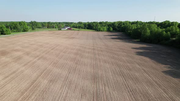 Aerial view of farm house and farm field with rows of plants under brght blue sky