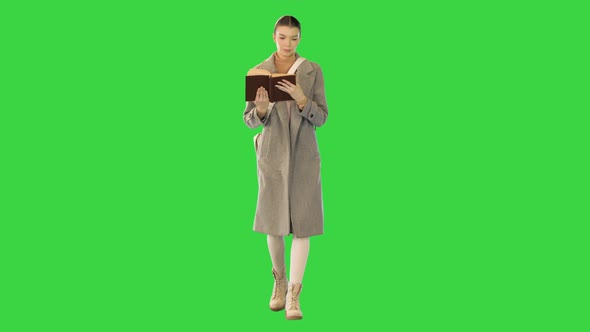 Young Woman in Stylish Clothes Walks Reading a Book on a Green Screen Chroma Key