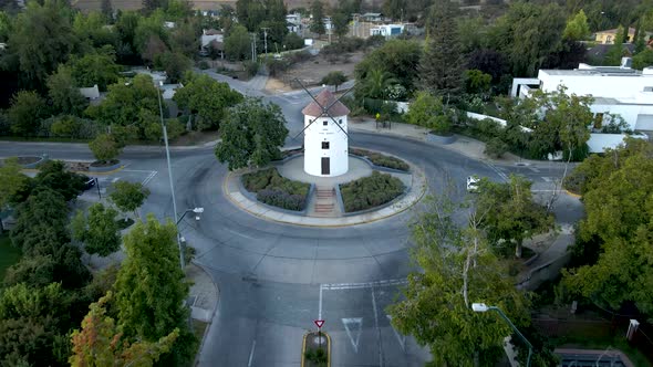 Aerial dolly out of Leonidas Montes windmill in roundabout with cars driving surrounded by trees, hi