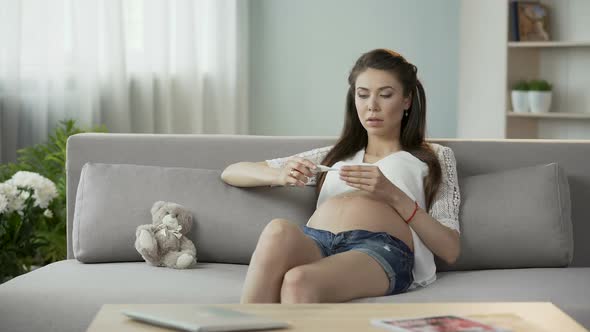 Young Pregnant Female Checking Body Temperature, Looking at Thermometer, Sad