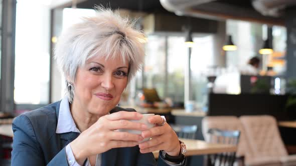 Business Middle Aged Woman Drinks Coffee in Cafe and Smiles To Camera - Closeup